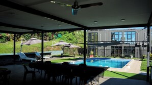 A covered patio with a pool, outdoor furniture, and a view of a modern house. - Hotel Laimoa (Apia)