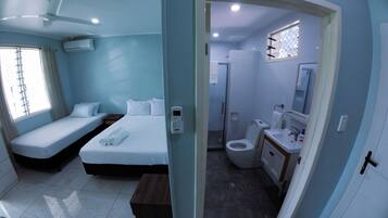 A hotel room with two single beds, a bedside table, an air conditioning unit, and a window with curtains.