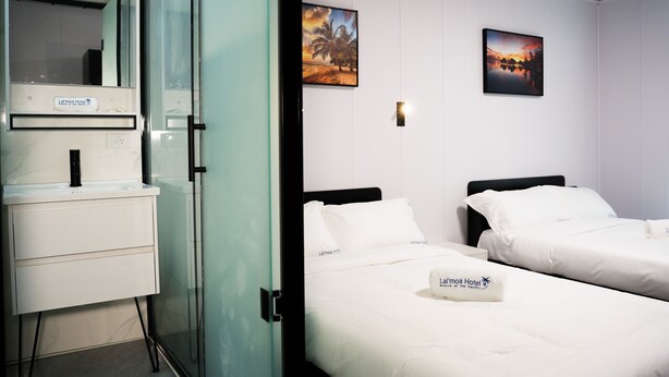 A hotel room with a glass partition, a white sink, two beds with white linens, and two framed pictures on the wall. - Hotel Laimoa (Apia)
