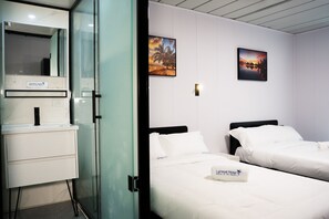 A hotel room with a glass partition, a white sink, two beds with white linens, and two framed pictures on the wall. - Hotel Laimoa (Apia)