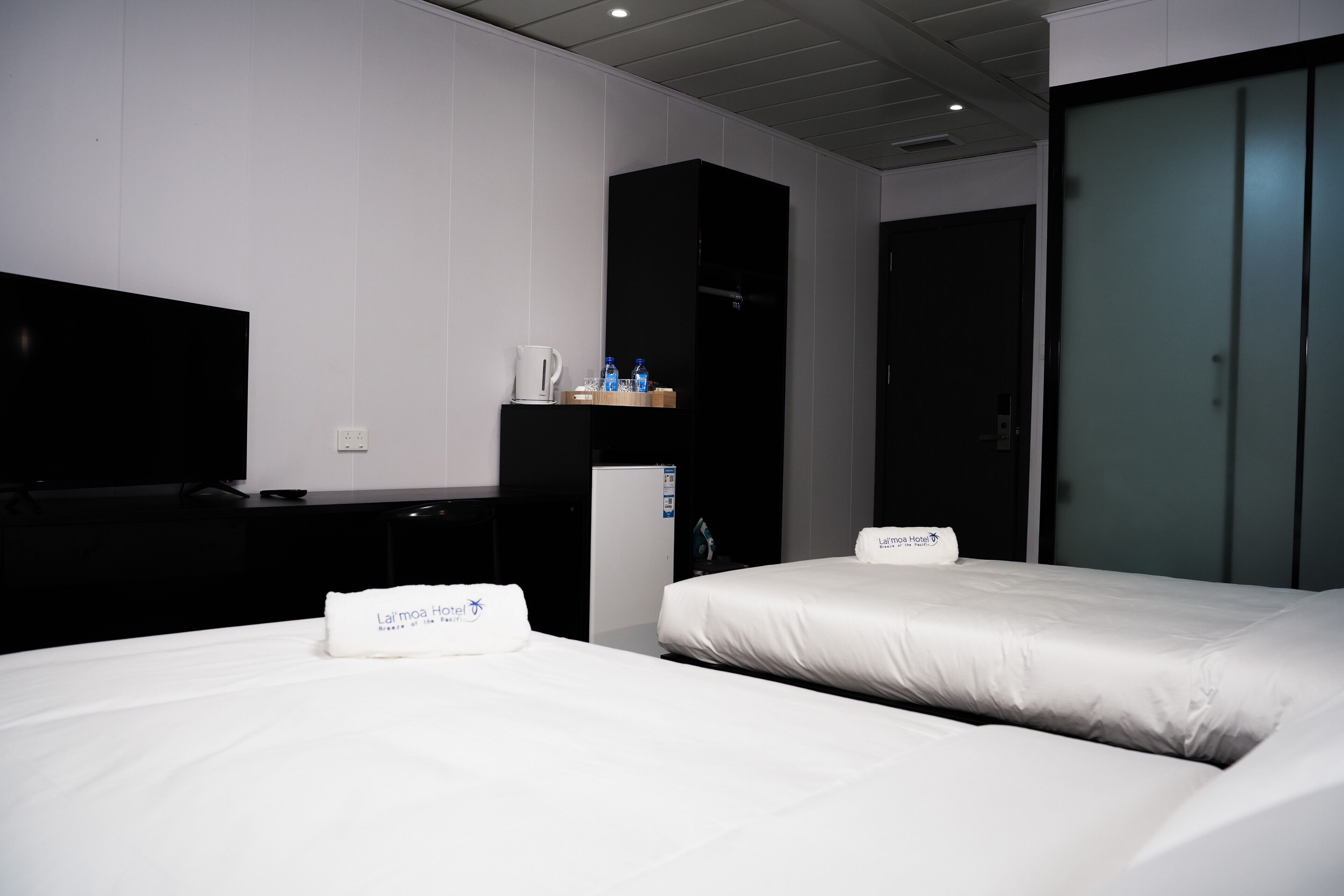 A hotel room with two beds, a TV, a minibar, and a wardrobe.