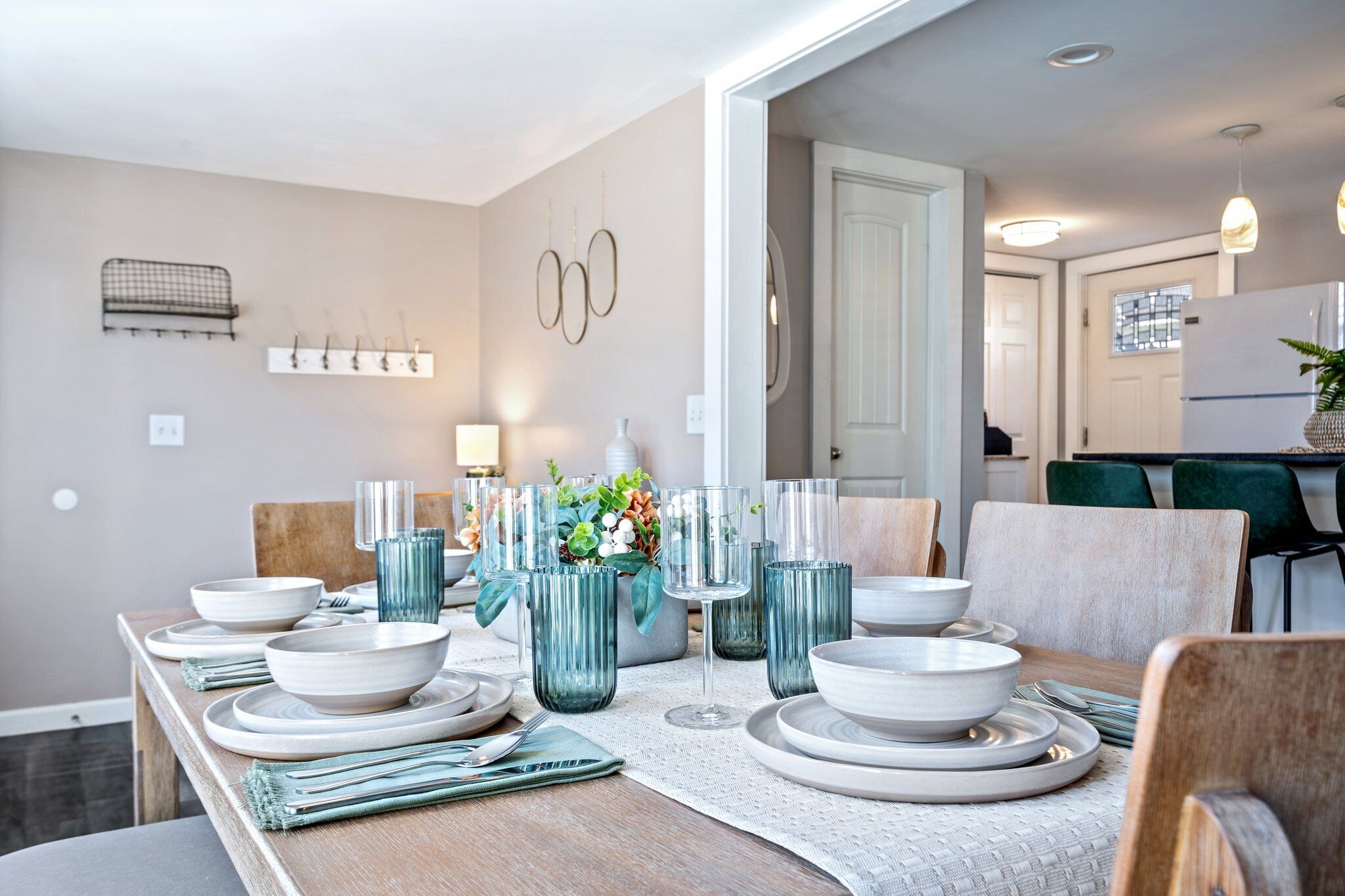 A dining area with a wooden table set for four, surrounded by chairs. There are decorative vases and a small plant on the table.