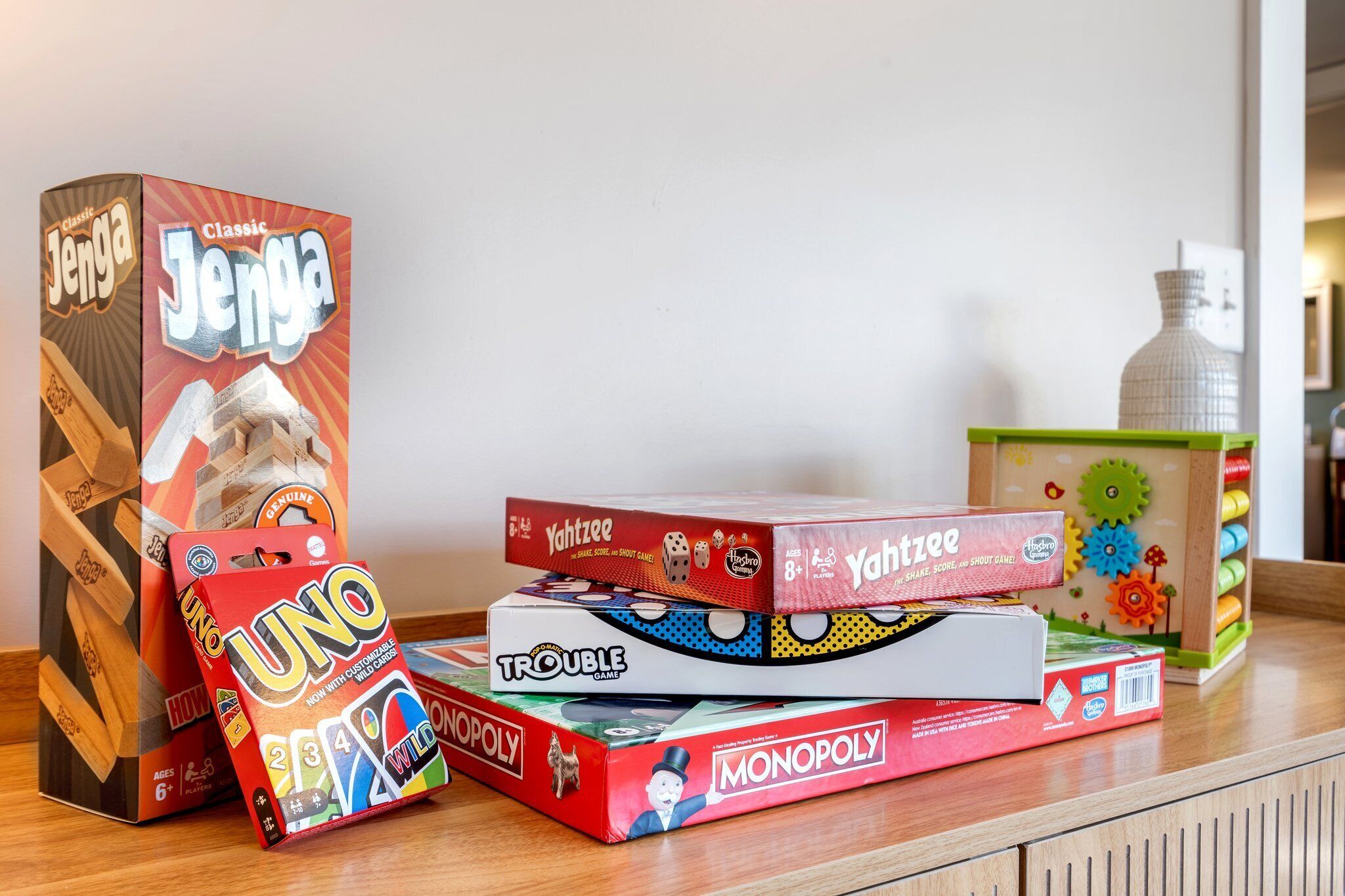 Una colección de juegos de mesa como UNO, Jenga, Yahtzee, Trouble y Monopoly sobre una superficie de madera.