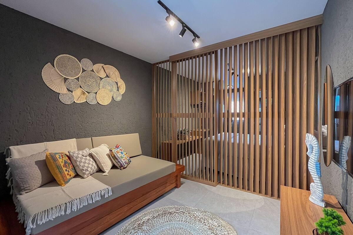 Un salon moderne avec un canapé, des œuvres d’art décoratives au mur, une cloison en bois et une petite plante en pot.