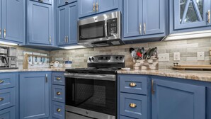 Een keuken met blauwe kastjes, roestvrijstalen apparatuur en een betegelde achterwand.