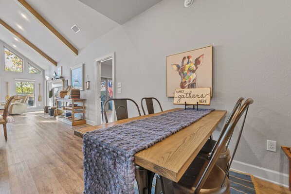 A dining area with a long wooden table, chairs, and a knitted table runner. - Relax in the Blue Cottage Retreat w/ lakefront views & walk down access to water (Clinton)