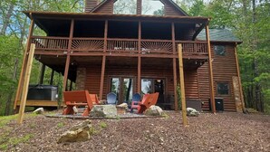 A wooden cabin with a balcony, outdoor seating, and a grill area.