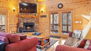 A log cabin interior with a fireplace, a television, and a cozy seating area.