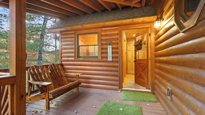 A wooden cabin with a porch, a bench, and a welcome sign.