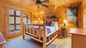 A wooden cabin bedroom with a bed, a ceiling fan, a nightstand, and a window with curtains.