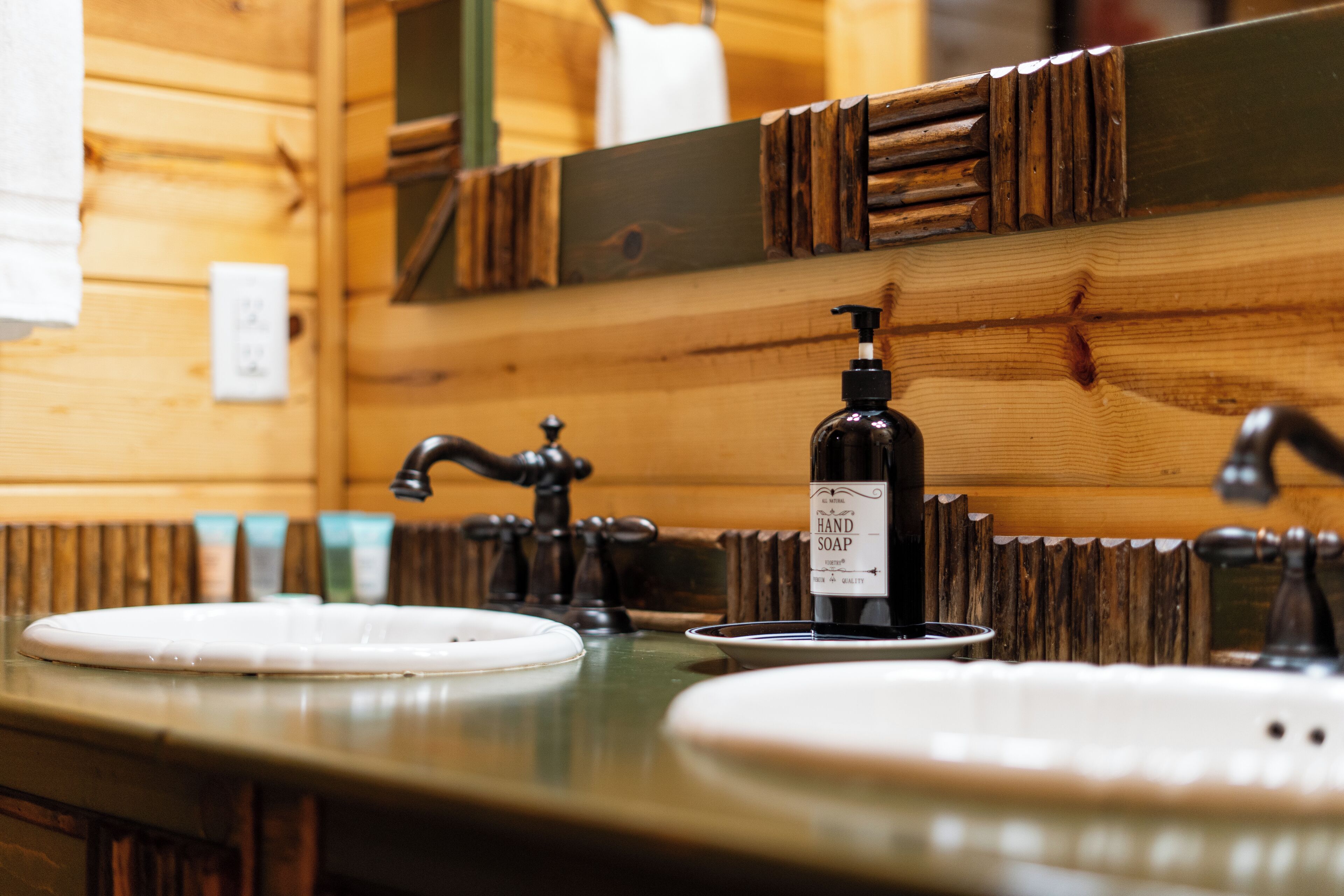 A wooden cabin-style bathroom with a wooden vanity, a hand soap dispenser, and a mirror with a wooden frame.