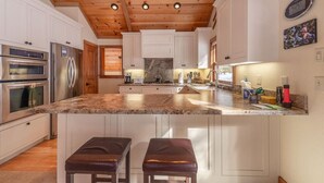 A kitchen with white cabinets, stainless steel appliances, a granite countertop, and wooden ceiling beams. - Super Clean - Tahoe Park Access! (Tahoe City)