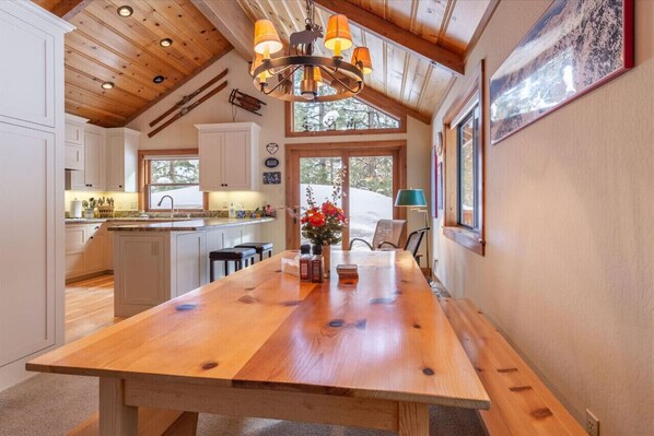 Una cocina amplia con una mesa de madera, armarios blancos y un ventanal grande.
