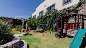 Un jardín con zona de juegos, que incluye un columpio y un tobogán, además de un muro de piedra.