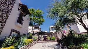 Una calle estrecha con edificios de piedra, una pérgola de madera y abundante vegetación.