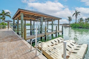 A wooden dock extending into a calm body of water, with a covered seating area and a boat docked nearby.