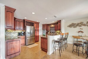 A modern kitchen with wooden cabinets, stainless steel appliances, and a bar area with stools.