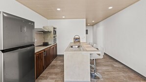 A modern kitchen with a stainless steel refrigerator, wooden cabinets, a built-in oven, and a central island with a sink and bar stools. - Apartment #3 -1-bedroom apartment with WiFi, AC in tranquil Tarcoles (Tarcoles)