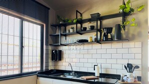 A modern kitchen with black countertops, white tiled backsplash, and black cabinetry. There are shelves with plants and kitchen items, a coffee machine, and a microwave. - Flat Itajuru (Cabo Frio)