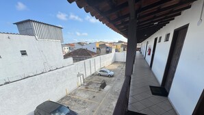 A parking area with a black SUV and a silver car, a white building with a corrugated metal roof, and a clear blue sky. - Flat Itajuru (Cabo Frio)