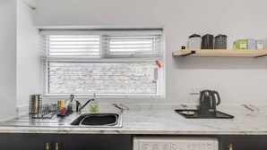 A compact kitchen with a built-in washing machine, a sink with dish racks, and a window with blinds.