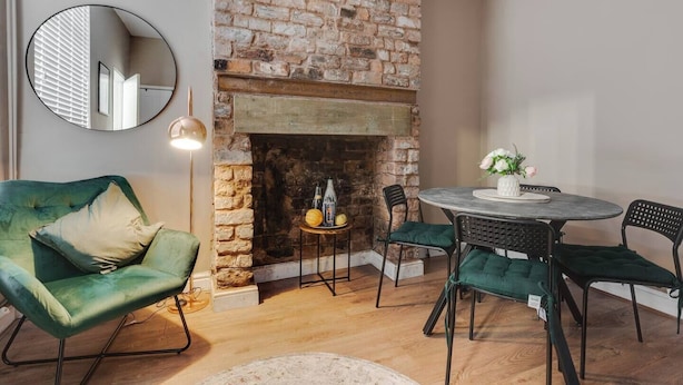 A cozy room with a brick fireplace, a round table with chairs, a green sofa, and a round mirror.