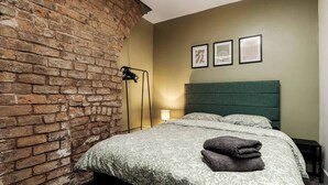 A hotel room with a brick wall, a bed with floral bedding, and three framed pictures on the wall.