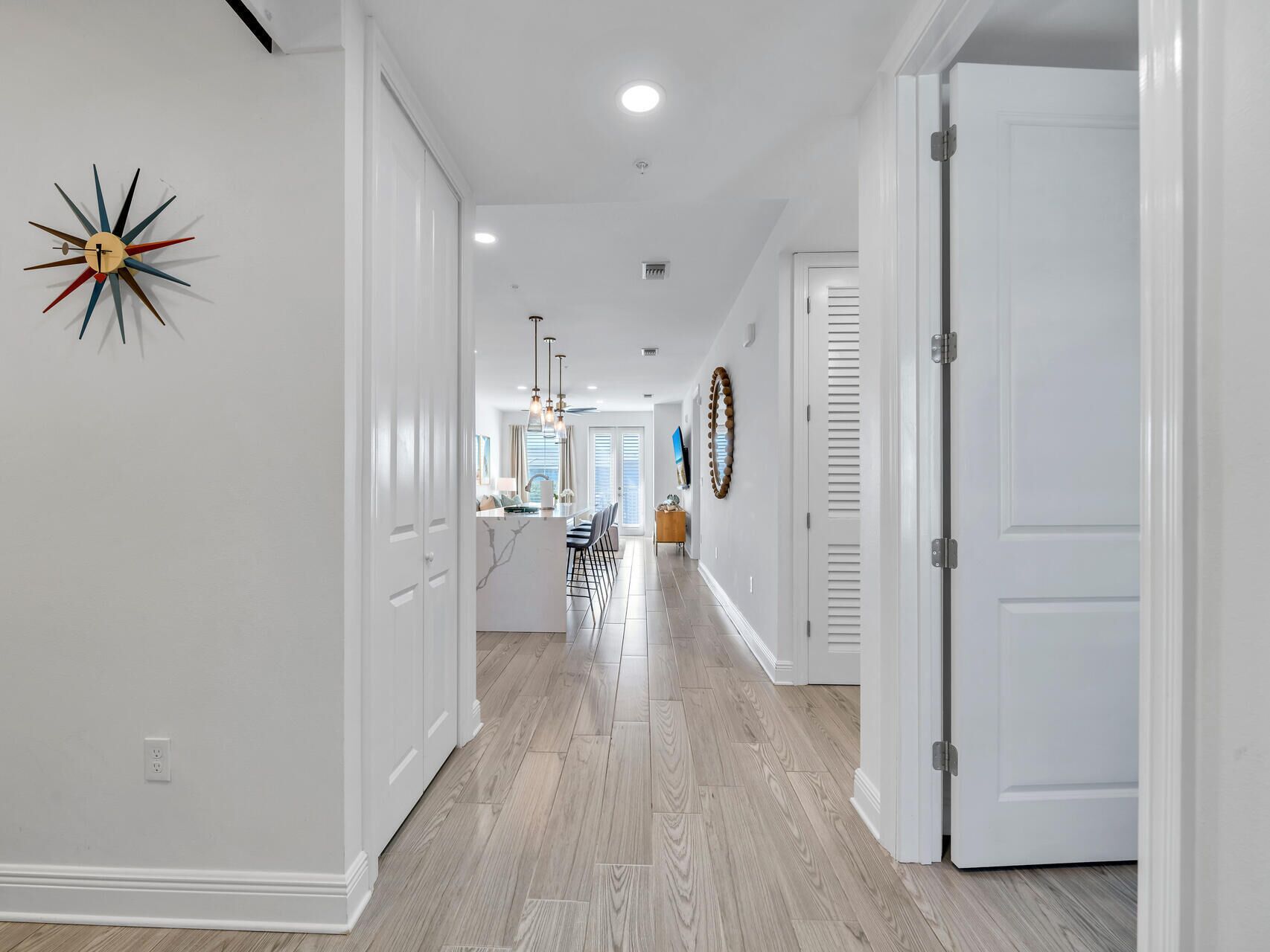 Un corridoio con pareti bianche, pavimento in legno e un lampadario moderno. Si apre una porta sulla destra e, alla sinistra, un elemento decorativo a parete.