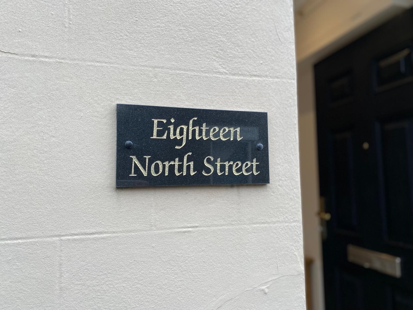 En svart skylt med vit text på en vit vägg, där det står ”Eighteen North Street”.
