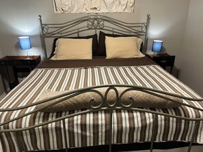 A neatly made bed with striped bedding, two bedside tables with lamps, and a decorative wall hanging above. - Charming 2-bedroom Cottage close to Lackland AFB, Seaworld, Alamo Downtown SA (San Antonio)