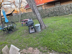 A grassy outdoor area with a barbecue grill, a trash can, and a picnic table. - Charming 2-bedroom Cottage close to Lackland AFB, Seaworld, Alamo Downtown SA (San Antonio)