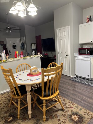 A dining area with a wooden table and chairs, a kitchen with white cabinets, a microwave, and a television. - Charming 2-bedroom Cottage close to Lackland AFB, Seaworld, Alamo Downtown SA (San Antonio)