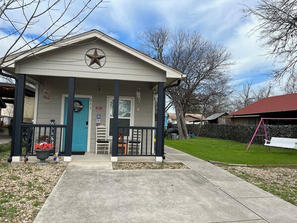 A small, single-story building with a porch, a welcome sign, and a mailbox. - Charming 2-bedroom Cottage close to Lackland AFB, Seaworld, Alamo Downtown SA (San Antonio)