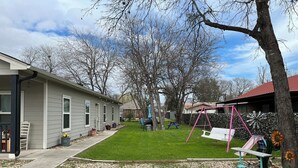 Patio trasero residencial con un columpio, una mesa de picnic y una casa de fachada gris.