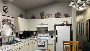 Cocina compacta con gabinetes blancos, estufa, refrigerador y una mesa de comedor con sillas.