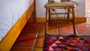 Un dormitorio con una cama de madera, una silla de madera con un objeto blanco encima y una alfombra estampada en el suelo.