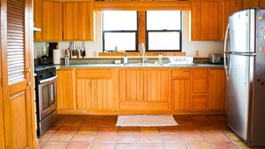 Una cocina con armarios de madera, un refrigerador de acero inoxidable, un ventanal y piso de baldosas.