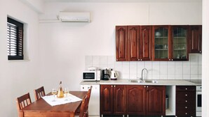 Una cocina compacta con armarios de madera, una encimera blanca, un microondas, una cafetera y una mesa de comedor preparada para dos personas, con copas de vino.