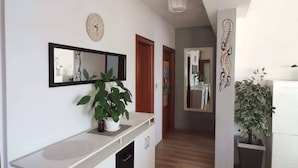Un couloir avec un lavabo blanc, un miroir, une horloge et une plante en pot.
