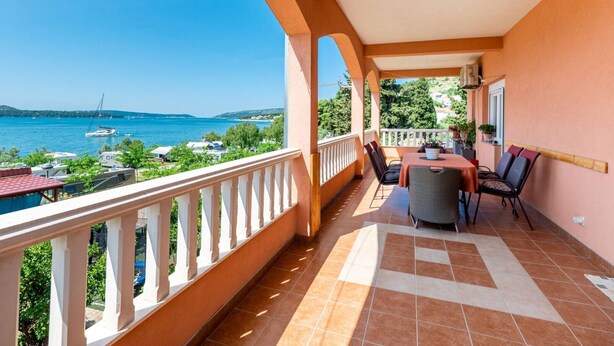 A balcony with a view of the sea, a table with chairs, and a potted plant.