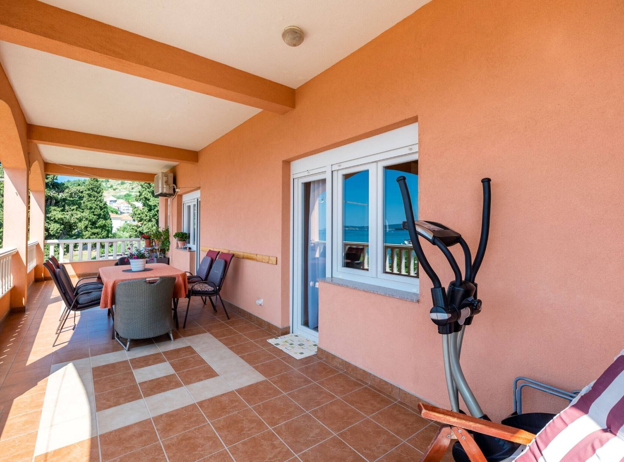 A covered patio with a table and chairs, a treadmill, and a view of the sea.
