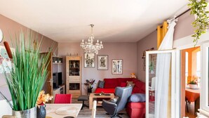 A modern living room with a red sofa, a chandelier, and a dining area with a red mat and a glass candle holder.
