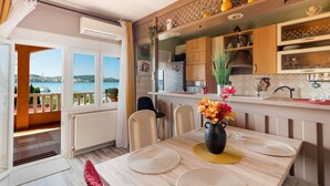 A modern kitchen with wooden cabinets, a dining table with placemats, and a view of the sea through large windows.