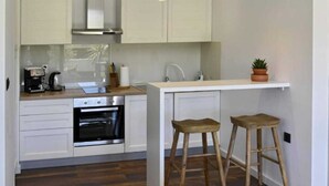 A compact kitchen with white cabinets, a built-in oven, a coffee maker, and two wooden stools.