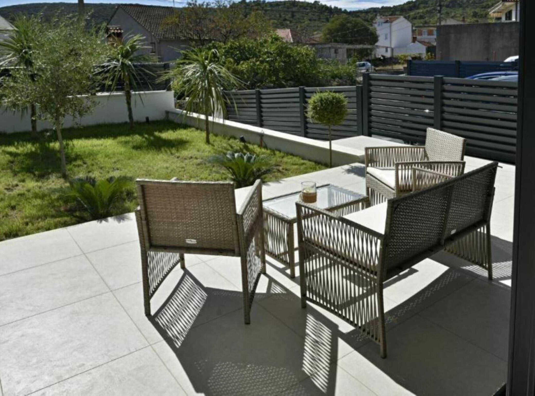 An outdoor patio area with a table and chairs, surrounded by a low fence and greenery.