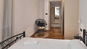 A bedroom with a bed, a chair, a small table, and a door leading to another room.