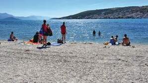 Une plage où des gens se prélassent au soleil et se baignent, un ciel dégagé et des collines lointaines.