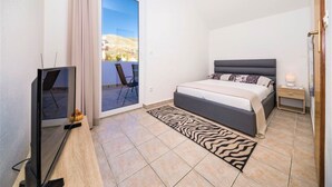 Une chambre à coucher comprenant un lit, une télévision, une petite table, une table de chevet et une vue sur un balcon avec une chaise.