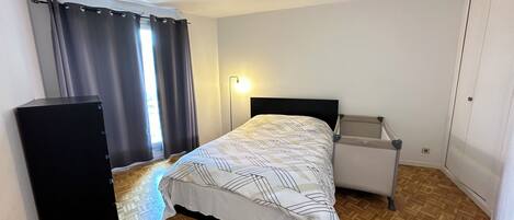 A bedroom with a bed, a bedside table, a lamp, a wardrobe, and a window with curtains.