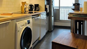 A compact kitchen with a washing machine, a coffee maker, and a microwave. - Spacious 2-room apartment with parking in Paris La Défense overlooking the Eiffel Tower   (Puteaux)